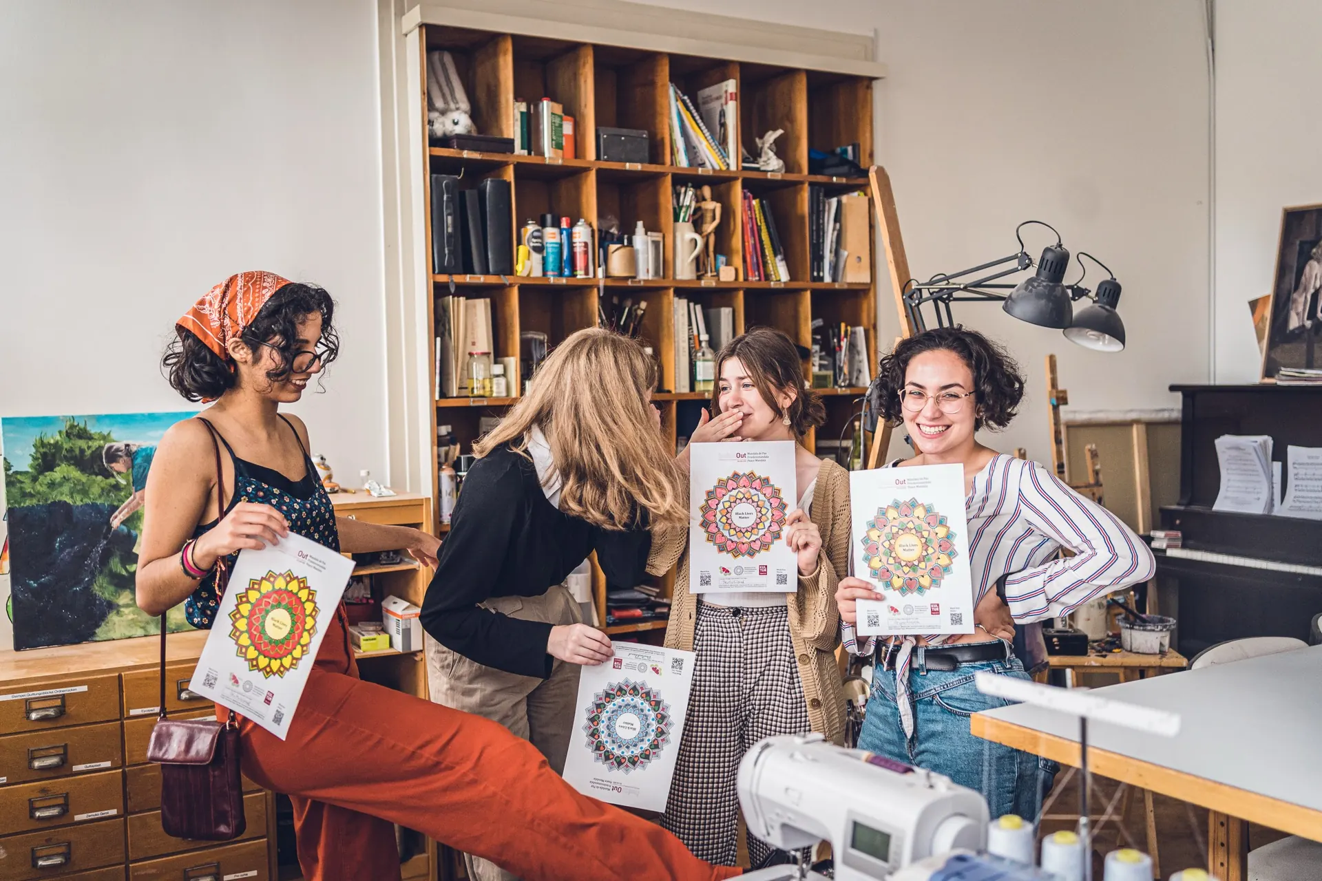 Four women stand laughing in the studio, holding up freshly made sheets.