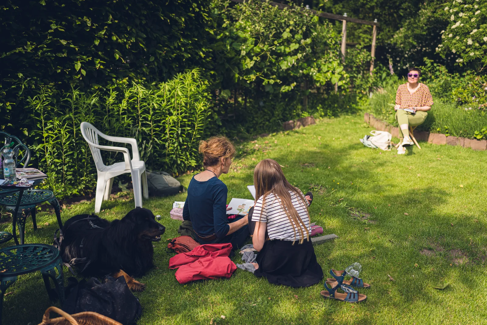 Kinder sitzen mit einer Decke im Garten, ein Hund liegt daneben.