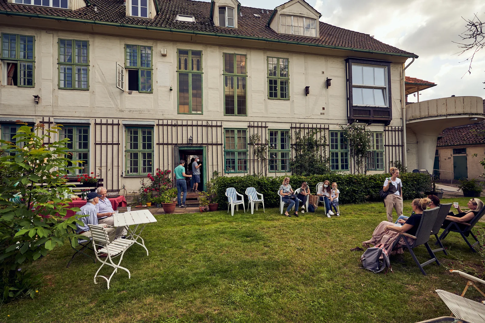 Menschen sitzen auf Gartenstühlen im Hof der Trift 32.