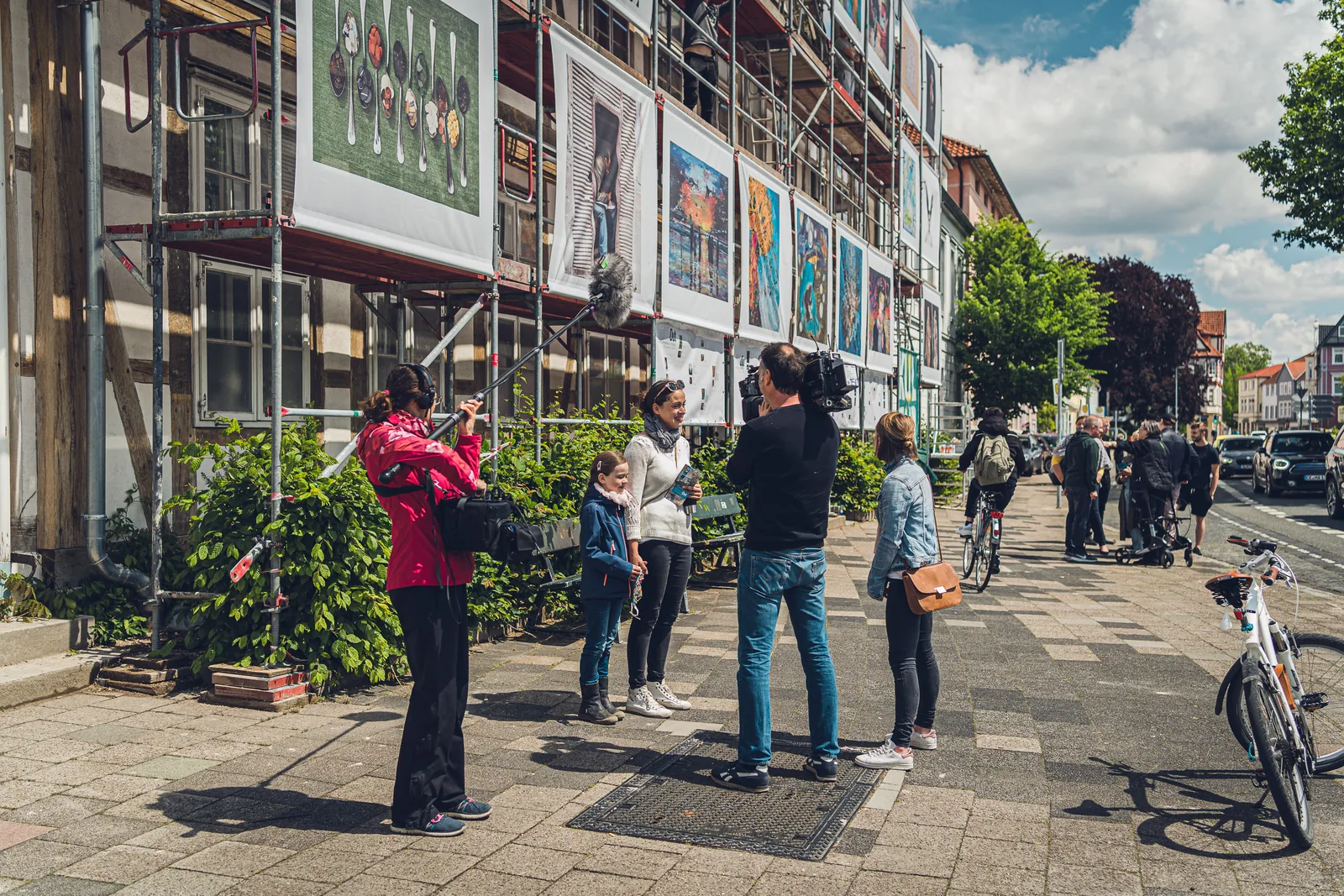 Menschen fotografieren von der Straße aus eine Hausfassade, die vollständig mit Bildern behängt ist.