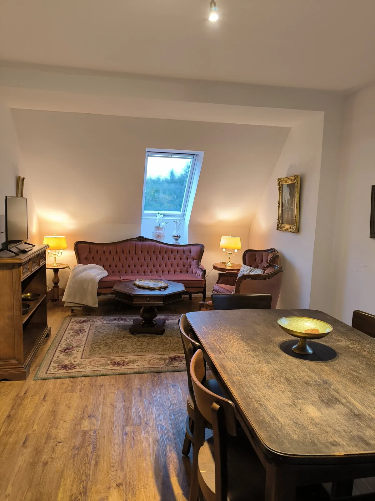 Wohnzimmer mit Sofa, Esstisch und warmem Lampenlicht.