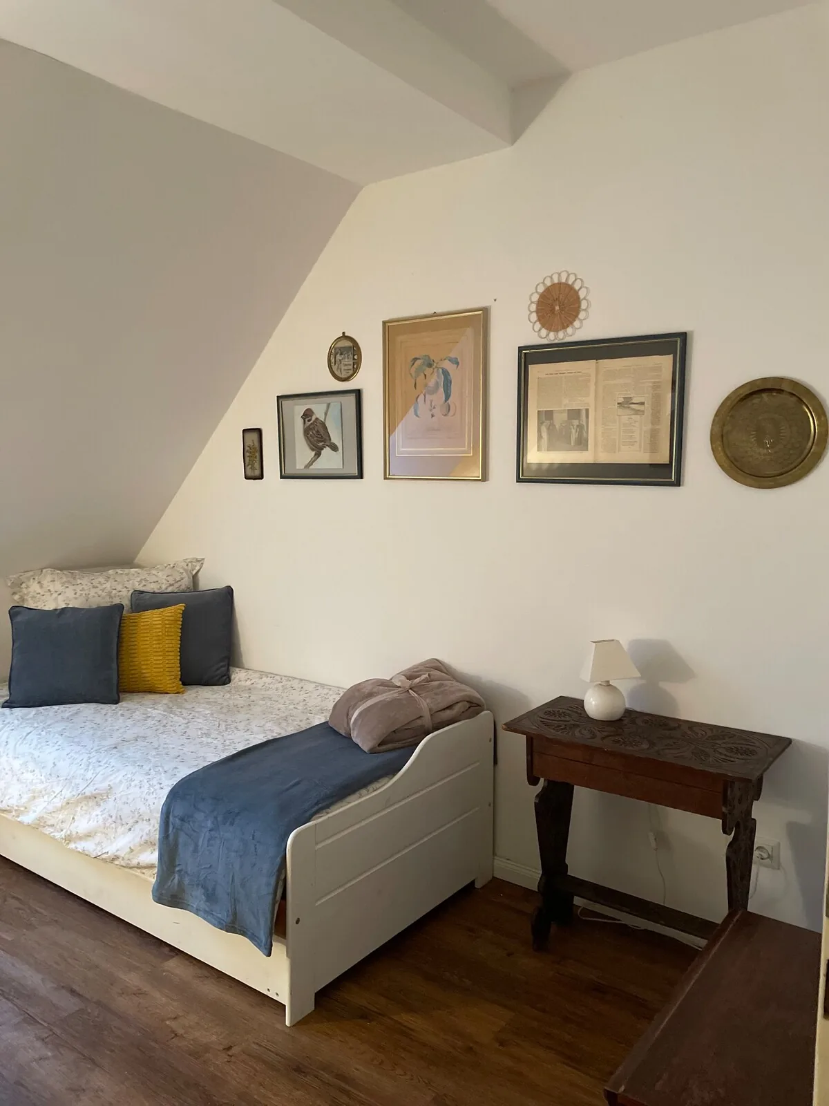 Zimmer unter der Dachschräge mit Bett und gerahmten Bildern.