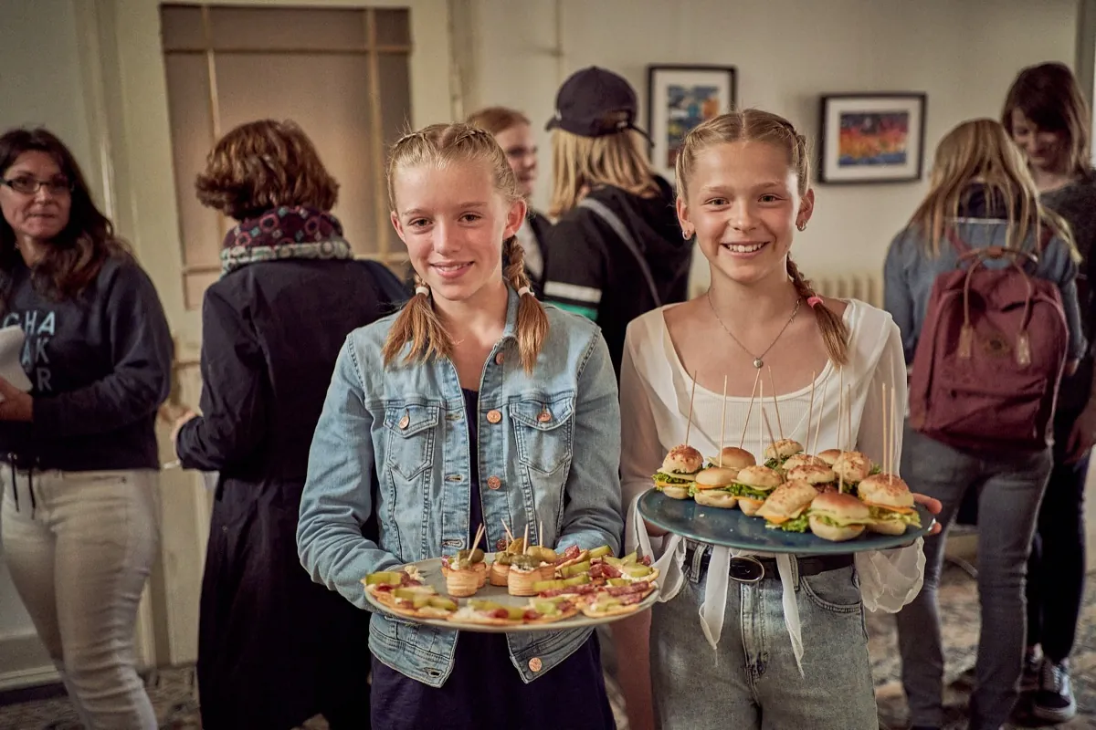 Two young women smiling as they carry a tray of food.