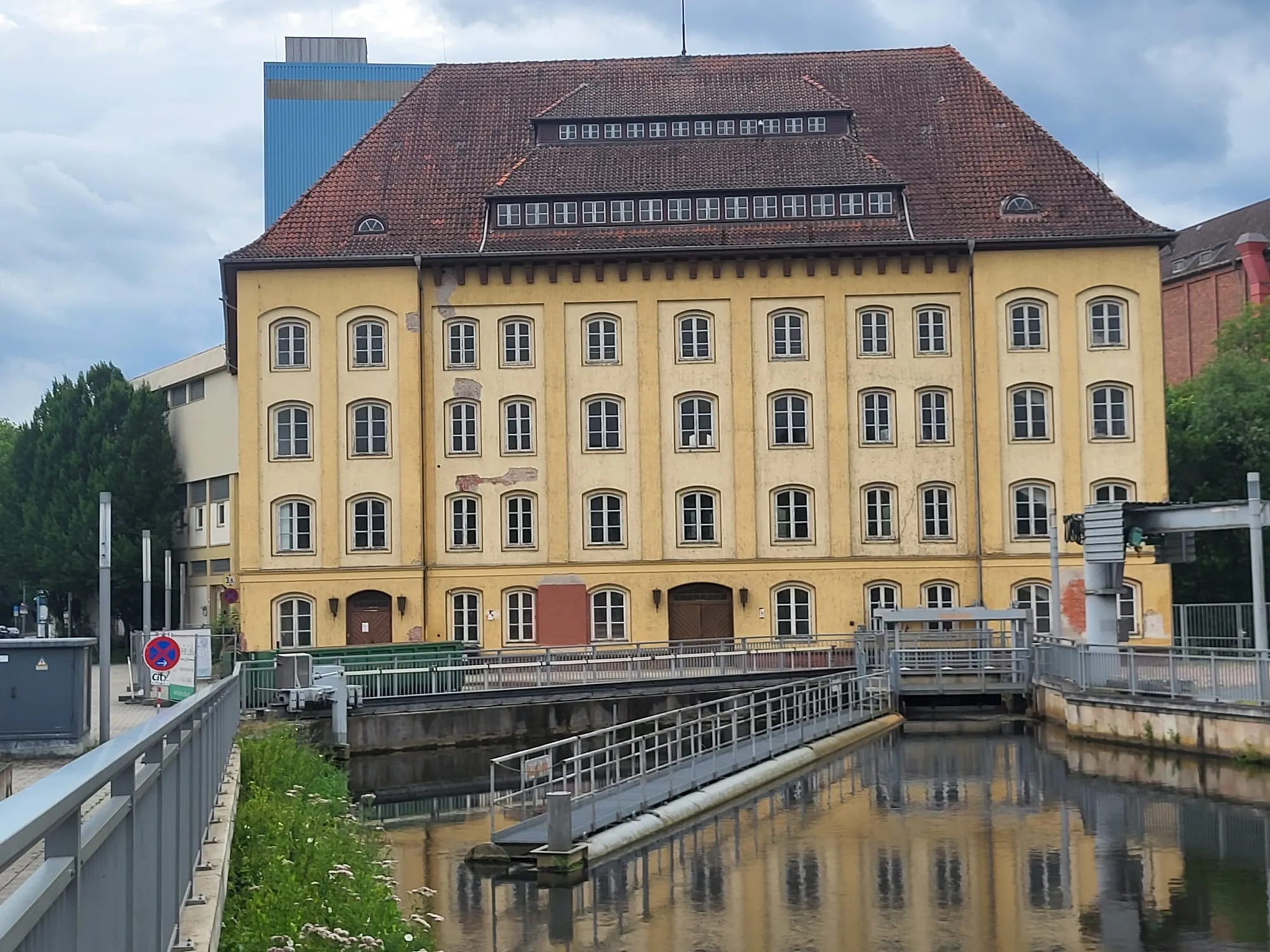 Das gelbe Gebäude der Rathsmühle Celle am Wasserlauf mit Wehr.